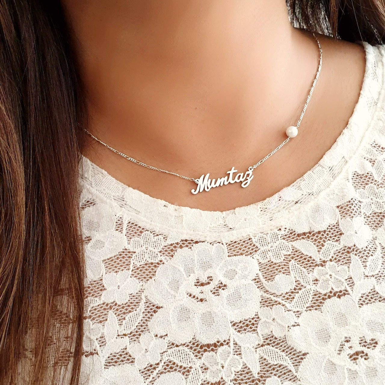 A woman wearing a customized name necklace with a pearl bead on a lace dress.